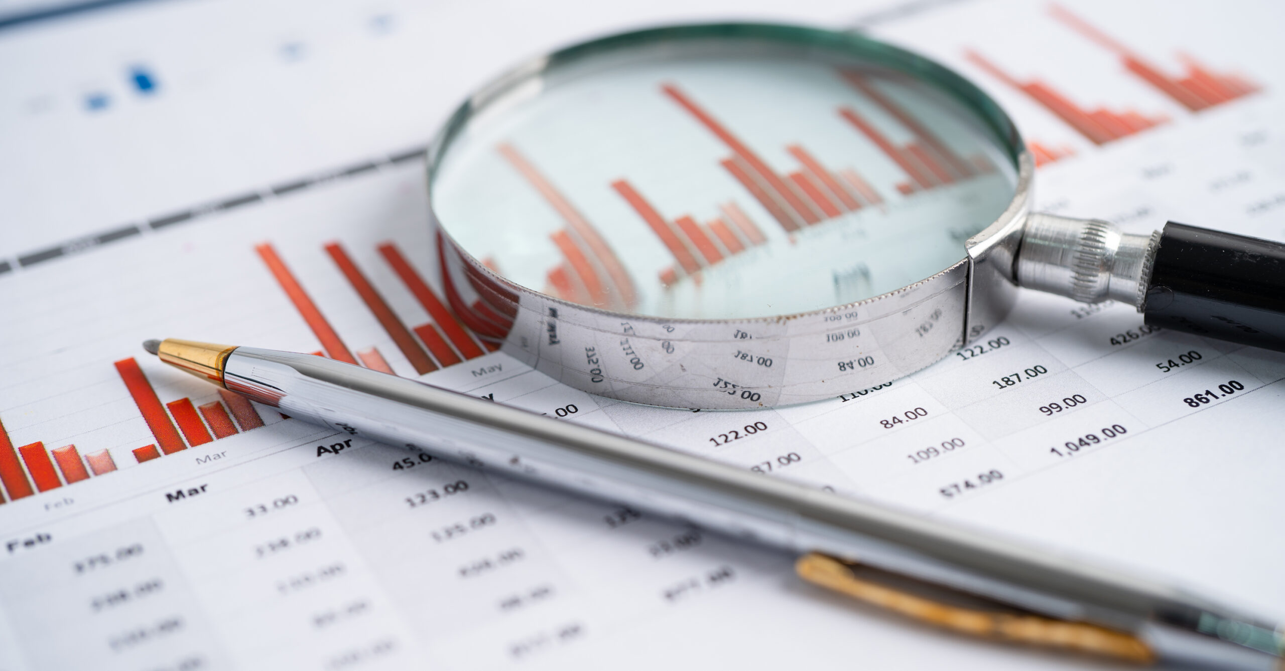 Close-up of financial documents with red bar charts, a ruler, and a magnifying glass for analysis.